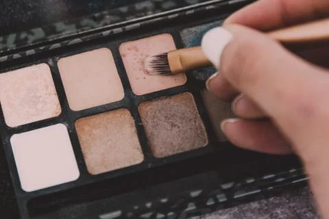Make-up brush tapping on eyeshadow with natural nude tone among other colors  Stock Photos