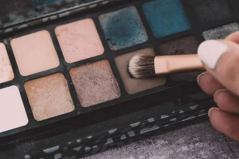 Make-up brush tapping on eyeshadow with natural nude tone among other colors  Stock Photos