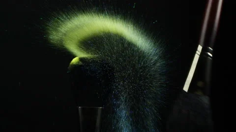 Make-up brushes with blue and yellow flying eye shadow powder particles on black Stock Footage 170358998
