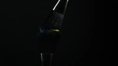 Make-up brushes with blue and yellow flying eye shadow powder particles on black Stock Footage 171903331
