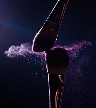 Make-up brushes with pink or violet powder explosion on dark background Stock Photos