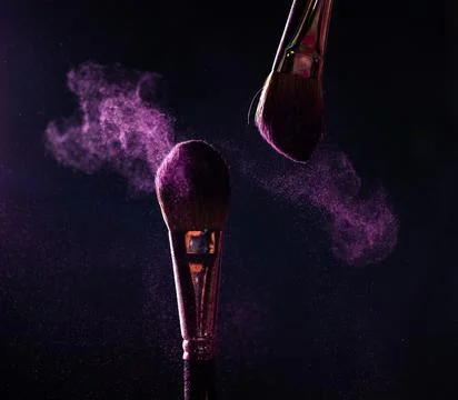 Make-up brushes with pink or violet powder explosion on dark background Stock Photos
