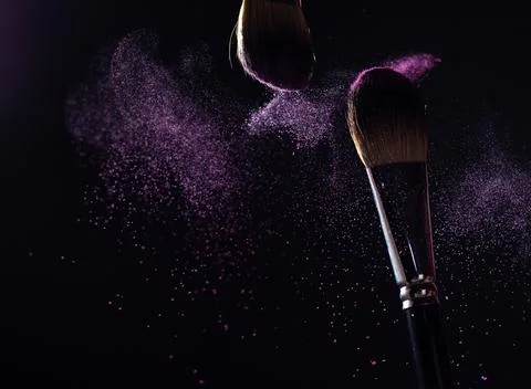 Make-up brushes with pink or violet powder explosion on dark background Stock Photos