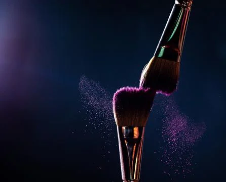 Make-up brushes with pink or violet powder explosion on dark background Stock Photos