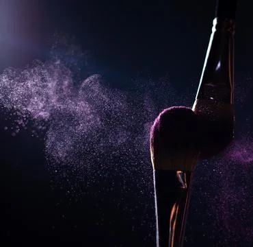 Make-up brushes with pink or violet powder explosion on dark background Stock Photos