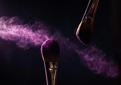 Make-up brushes with pink or violet powder explosion on dark background Stock Photos