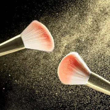 Make-up brushes with powder on it and heap of golden powder on black backgr.. Stock-Fotos