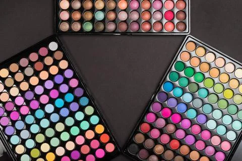 Make-up frame made of colorful eyeshadow palettes arranged as triangle on black Stock Photos
