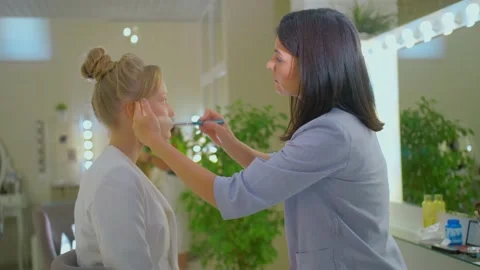A make-up girl puts makeup on a blonde , two girls do makeup, a professional Stock Footage 136507301