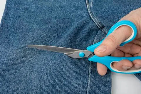 Make a hole in blue jeans with scissors Stock Photos
