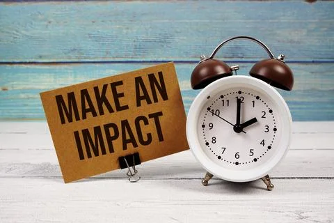 Make An Impact text written on paper card with alarm clock on wooden backgrou Stock Photos