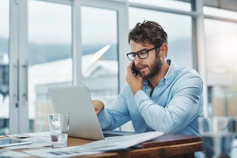 Make it happen with multitasking. a young businessman using a phone and laptop Stock Photos