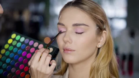 Make-up master holds in her hands a color palette with shadows and makes a Stock Footage 236118460