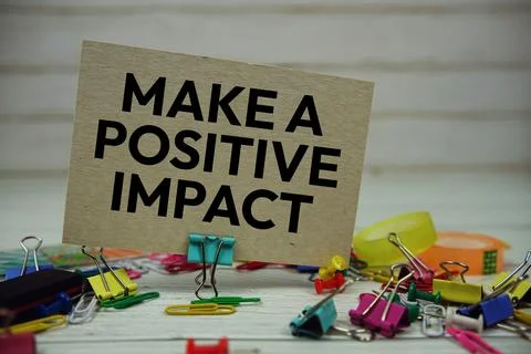 Make A Positive Impact text on paper card with stationary on wooden backgroun Stock Photos