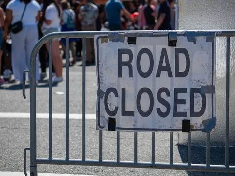 Make shift road closed sign hanging on barrier with crowd in back Stock Photos