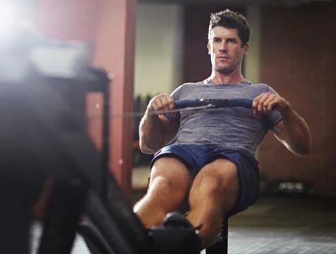 Make those muscles work. a young man working out on a rowing machine in a gym. Stock Photos