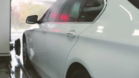 Make worker washing side doors of white car under high pressure water after foam Stock Footage 129303605