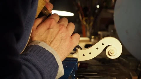 Maker using small sharp chisel to clean edges of violn scroll pegbox area and Stock Footage 319483178