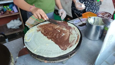 Makes a crepe pancake on a baking tray in a creperie, give chocolate topping Видео 204048852