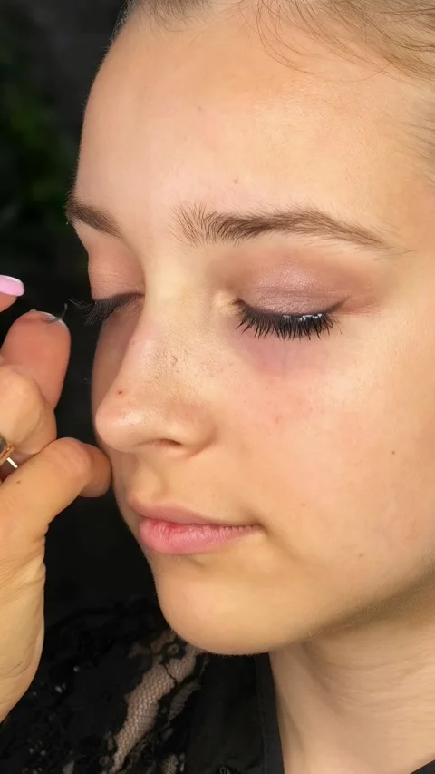 Makeup artist applies false eyelashes to a teenage girl in close up Stock Footage 342333458