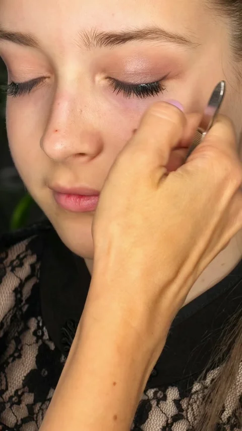 Makeup artist applies false eyelashes with tweezers to a teenage girl Stock Footage 344532577