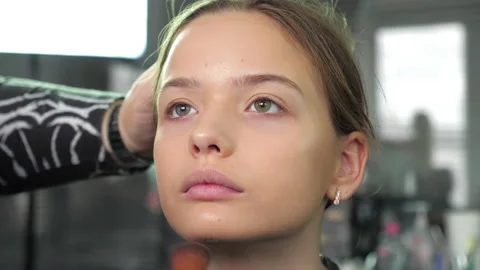 Makeup artist applies foundation on face with brush to teenager girl in salon Stock Footage 133802450