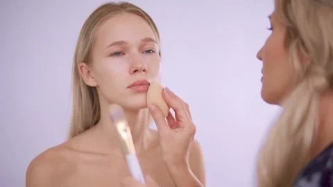 The makeup artist applies the foundation to the model Stock Footage 142134896