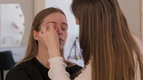 Makeup Artist applies foundation with sponge on a girl model, corrects skin tone Stock Footage 199839074