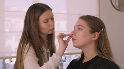 Makeup Artist applies foundation with sponge on a girl model, corrects skin tone Stock Footage 199839096