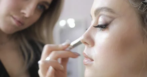 Makeup artist is applying blush bronzer using brush to young model cheek. Stock Footage 145504100