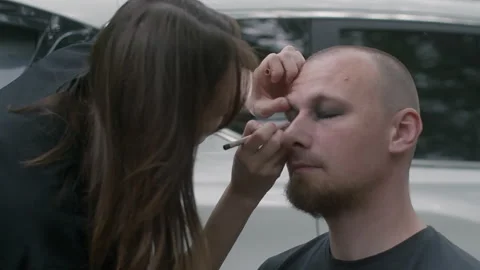 Makeup artist applying dramatic eye makeup to man outdoors Stock Footage 340651578