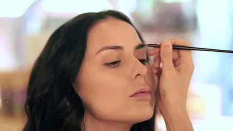 Makeup artist applying filling in eyebrows of a model with eyeshadows Stock Footage 76018669