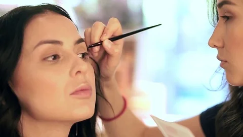 Makeup artist applying filling in eyebrows of a model with eyeshadows 動画素材 76018679