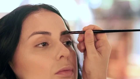 Makeup artist applying filling in eyebrows of a model with eyeshadows Stock Footage 76018684