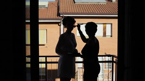 Makeup artist applying make upthe bride. Silhouette against a red house Stock Footage 46241488