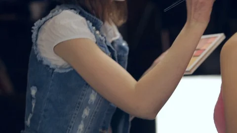 Makeup artist applying makeup with a brush on face of young woman. Panning Stock Footage 72131814