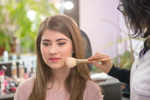 Makeup artist applying makeup to model in salon. Stock Photos