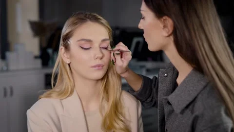 The makeup artist attaches false eyelashes to the client with tweezers and glue Stock Footage 236472605