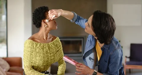 Makeup artist blending blush across African American client cheeks at home after Stock Footage 341467572