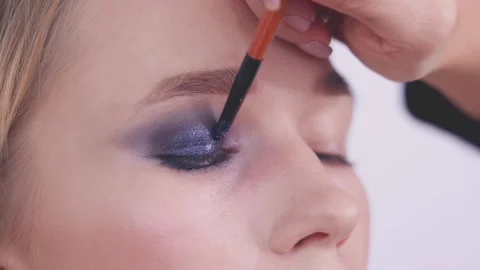 The makeup artist blends eyeshadow onto the model's eye. Stock Footage 142135416