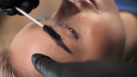 A makeup artist brushes the eyebrows of a young girl with healthy face skin  Stock Footage 198881014