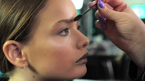 Makeup artist combing eyebrows using a brush to a teenager girl in beauty salon Stock Footage 134231570