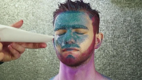 Makeup artist covering young man's face with the sparkles slow motion Stock Footage