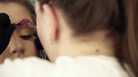 Makeup artist fixing the shape of eyebrows for a young woman Stock Footage 73673795