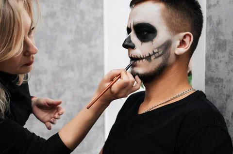 A makeup artist makes a demon makeup for a young man in a beauty salon Stock Photos