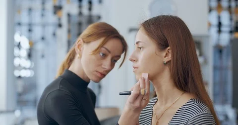 Makeup artist makes makeup to young girl and applies a cream Stock Footage 126129394