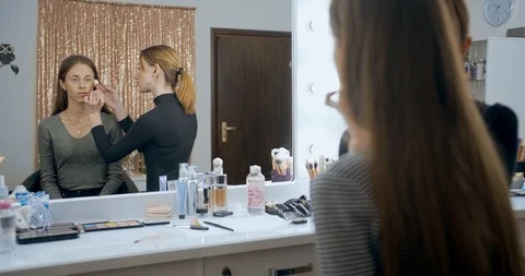 Makeup artist makes makeup to young girl face and applies a color sculpting Stock Footage 126180789