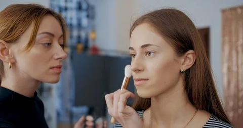 Makeup artist makes makeup to young girl face and applies a color sculpting Видео 126181195