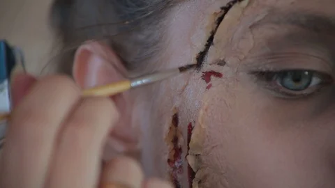 Makeup artist makes wax plastic makeup in form of bloody wound on face of girl Video stock 105599884