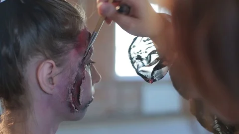 Makeup artist makes wax plastic makeup in form of bloody wound on face of girl Video stock 105600026